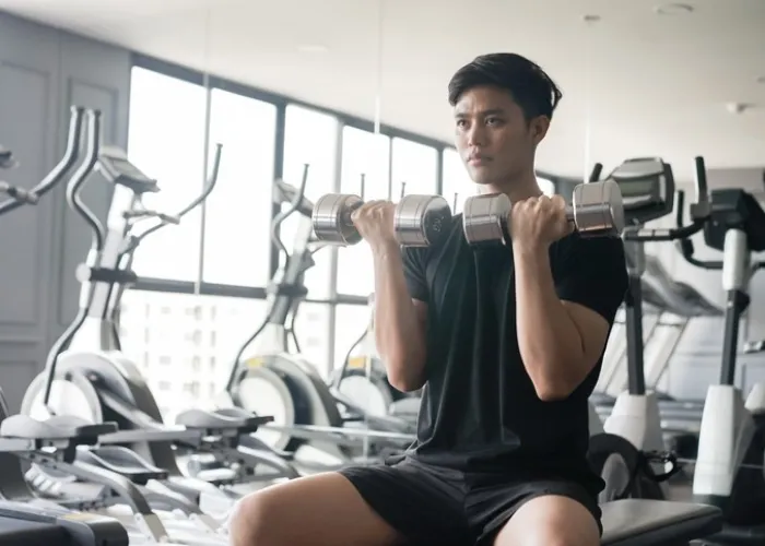 close up young asian man holding dumbbell in hand for playing shoulder press to gaining muscle at gym in the afternoon , healthy lifestyle concept
