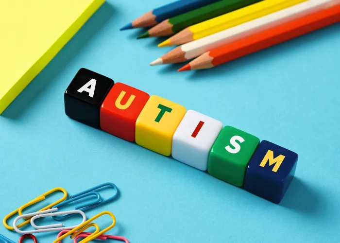 Autism and education concept. Autism spectrum disorder. The word autism on colorful cubes with stationery objects on blue background.