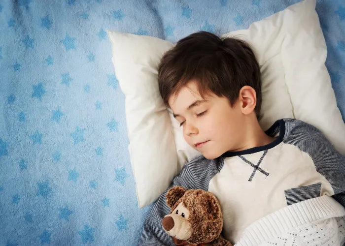 six years old child sleeping in bed on pillow with alarm clock and a teddy bear