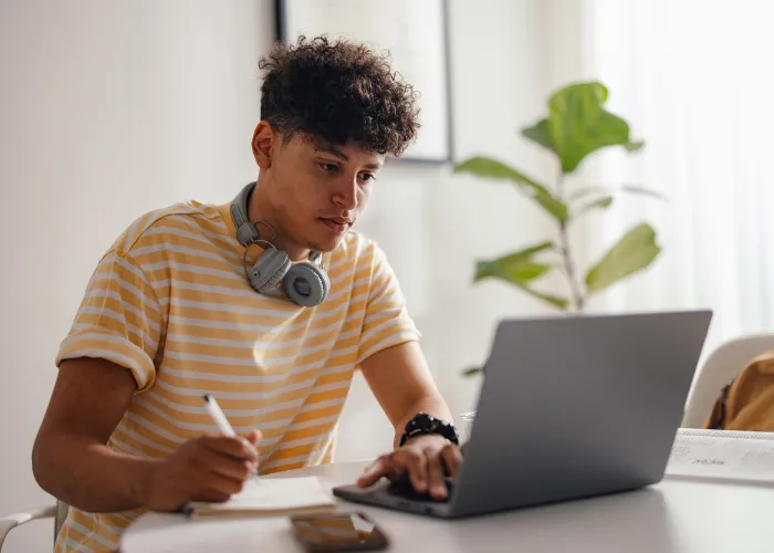 Young Man Studying at Home with Headphones and Laptop