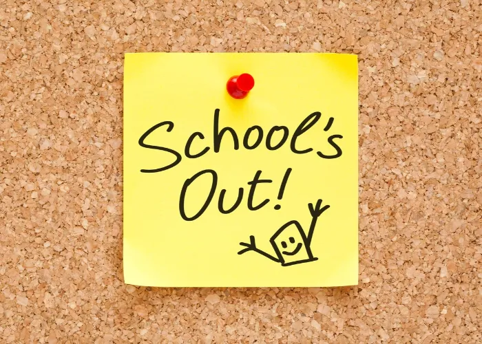 School is Out handwritten on a sticky note pinned on cork bulletin board.
