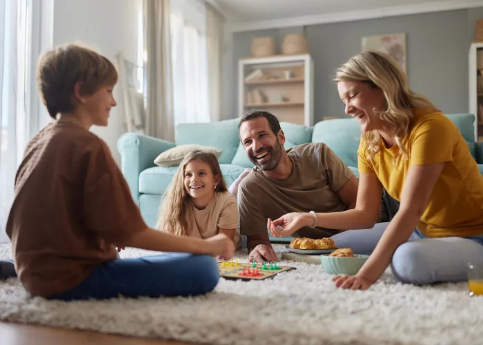 Happy family having fun while playing Ludo game on carpet in the living room. Focus is on father and daughter.