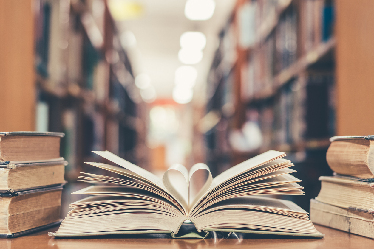 Love story book with open page of literature in heart shape and stack piles of textbooks on reading desk in library, school study room for national library lovers month and education learning concept
