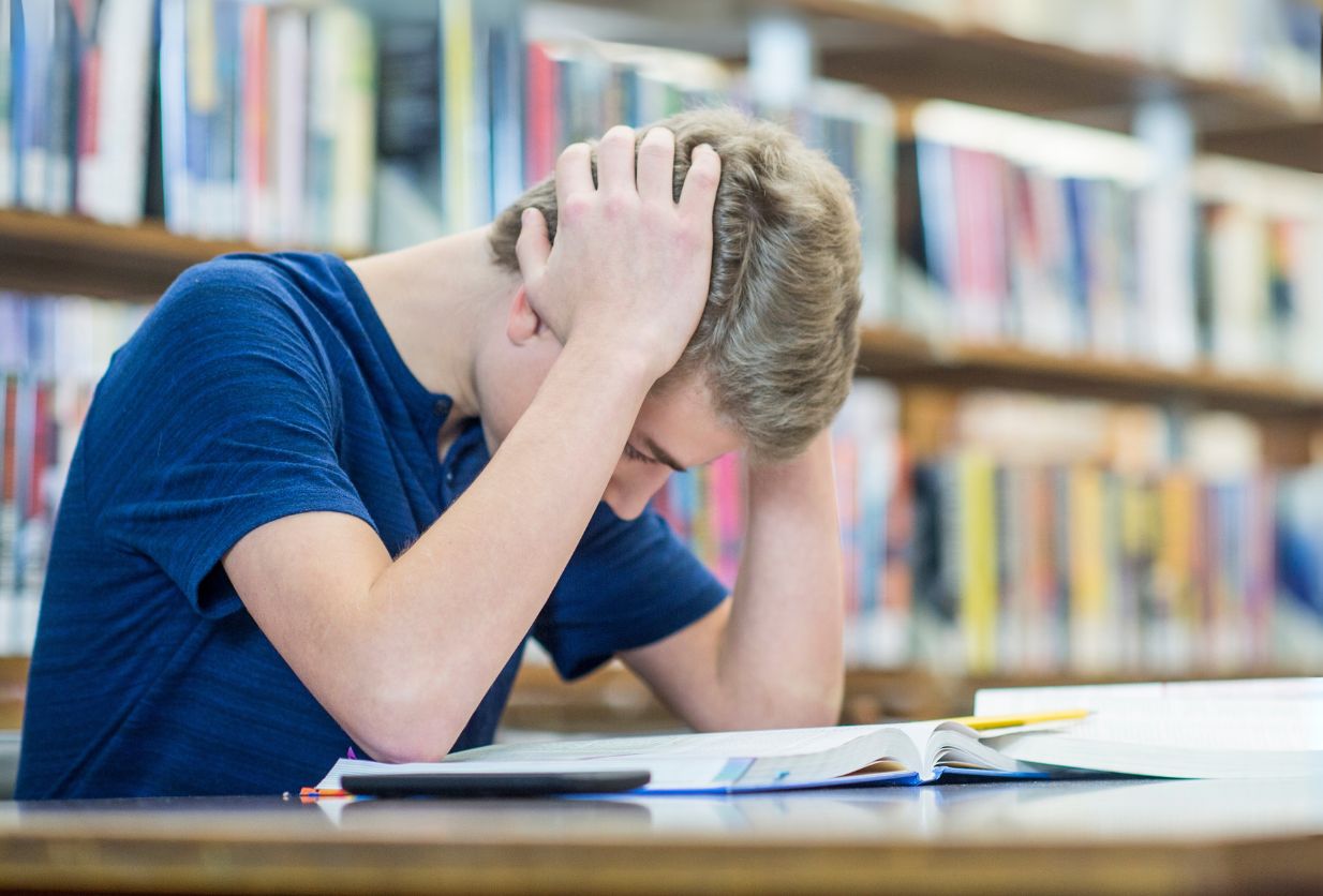 Teenager holding head in library while studying