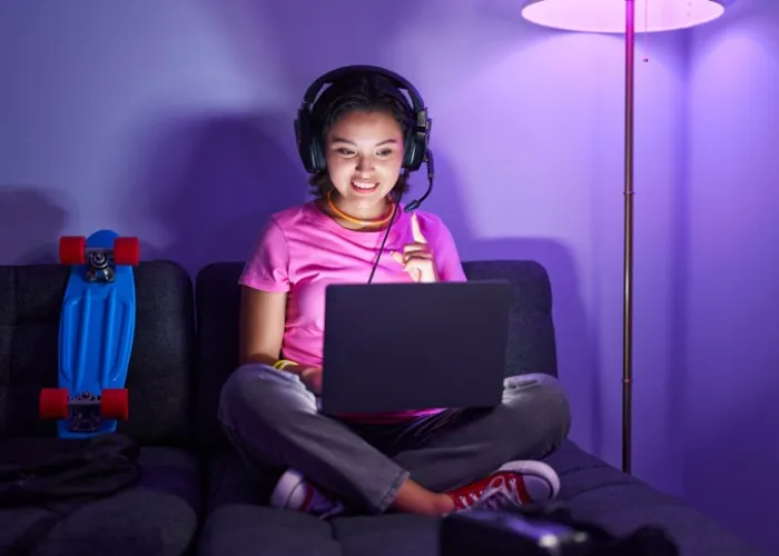 Hispanic young woman playing video games sitting on the sofa smiling happy pointing with hand and finger