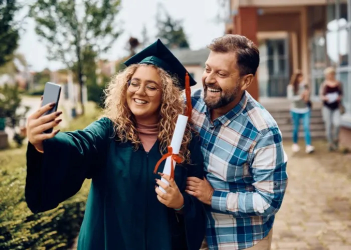 Happy student taking selfie with her father on her graduation day.